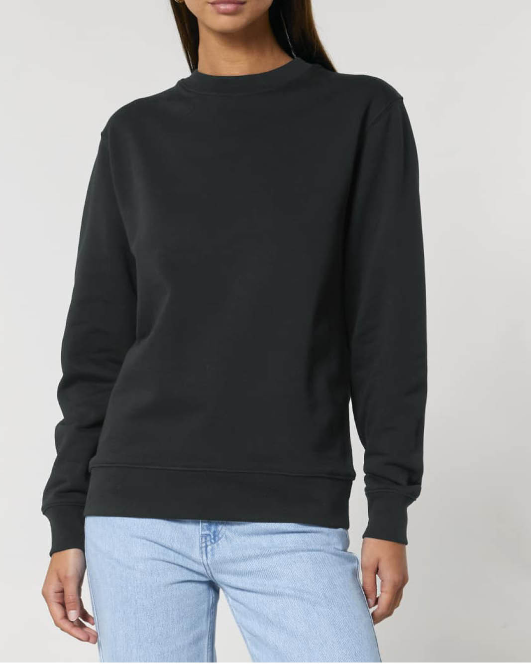 A woman wearing a plain black long-sleeve crewneck sweatshirt showcasing it's cuffed sleeves, waist and neckline.
