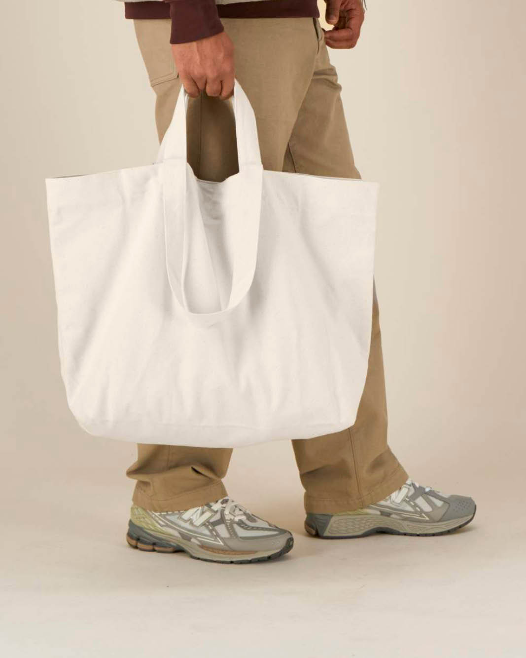 A person holding a large  oversized natural canvas tote to show how large the tote bag is.