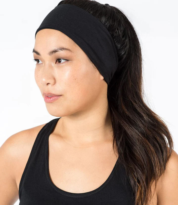 A woman wearing a wide, black athletic headband with her hair tied back in a ponytail, shown in a side profile to show the use of the fitness headband.