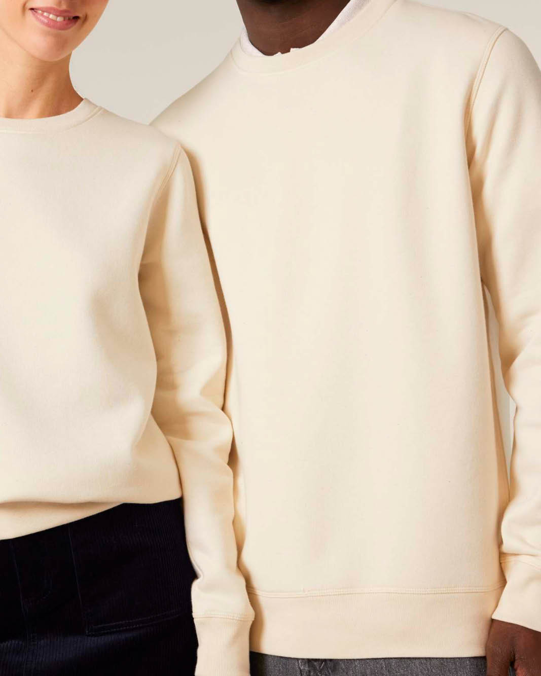 Two models wearing plain cream-colored crewneck sweatshirts, cropped from the chest down